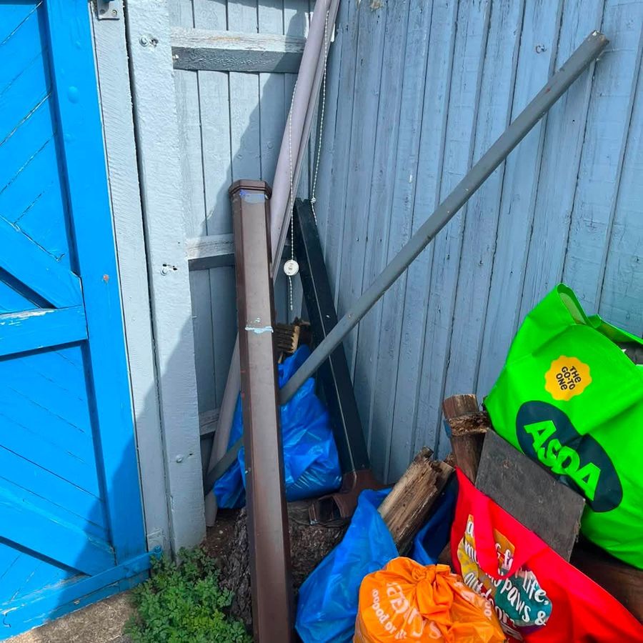 Household bags and timber stacked in a side passage before a Castle Vale clearance
